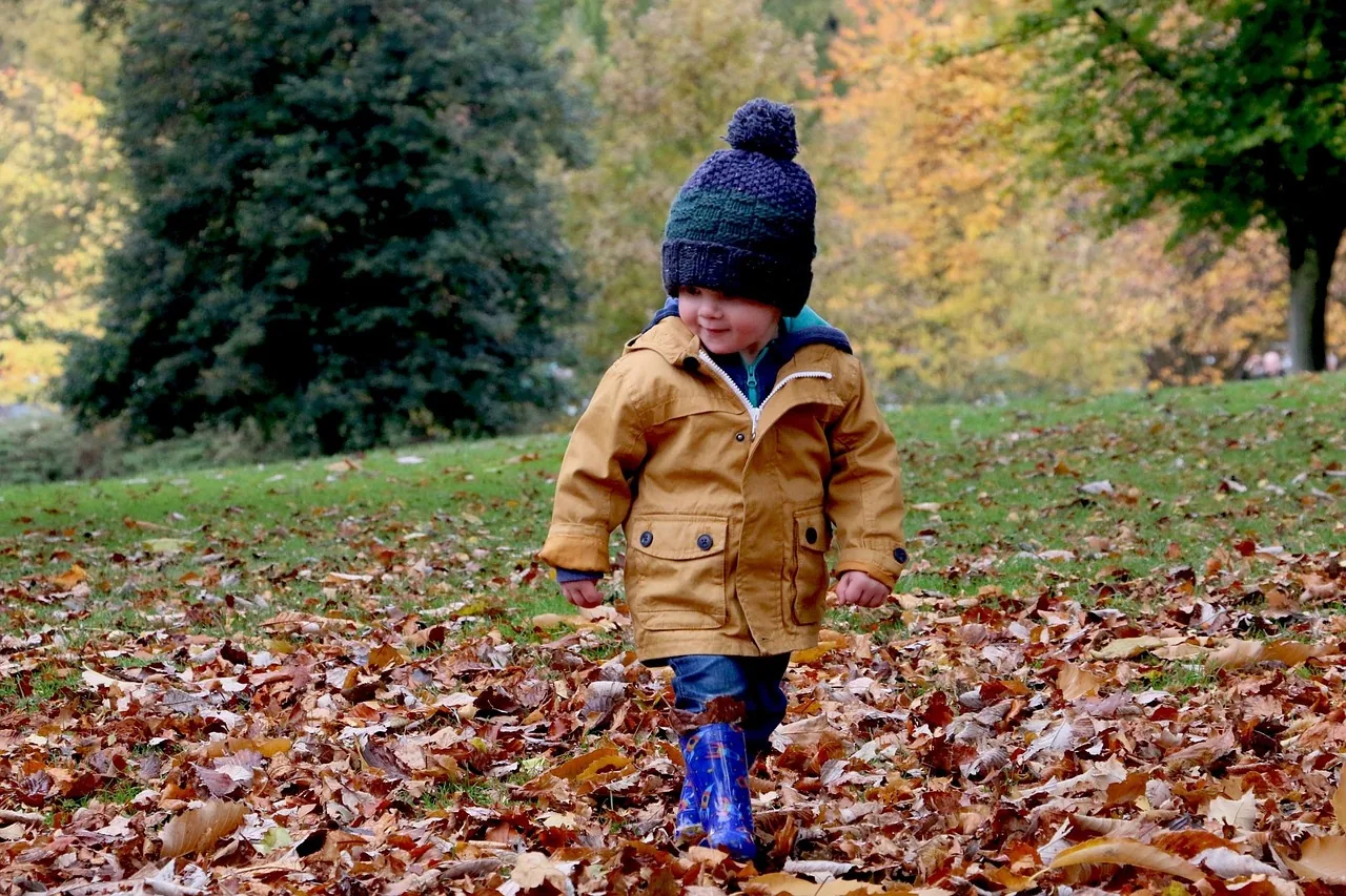A child in a coat and hat walking through fallen leaves