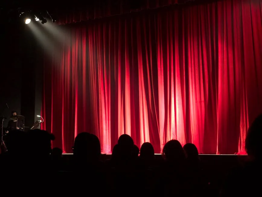 A theatre audience facing a stage with red curtains