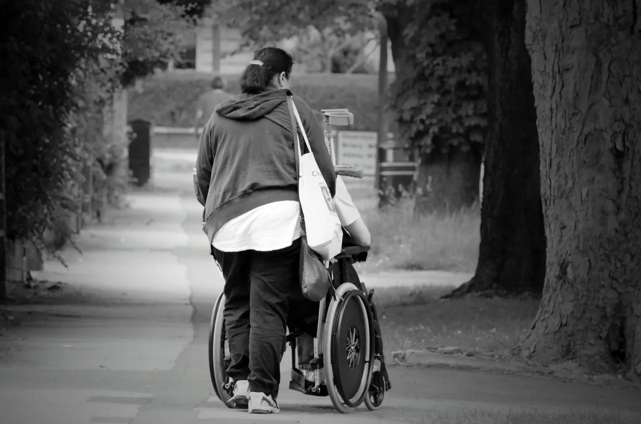 A person walking behind a wheelchair user on a path