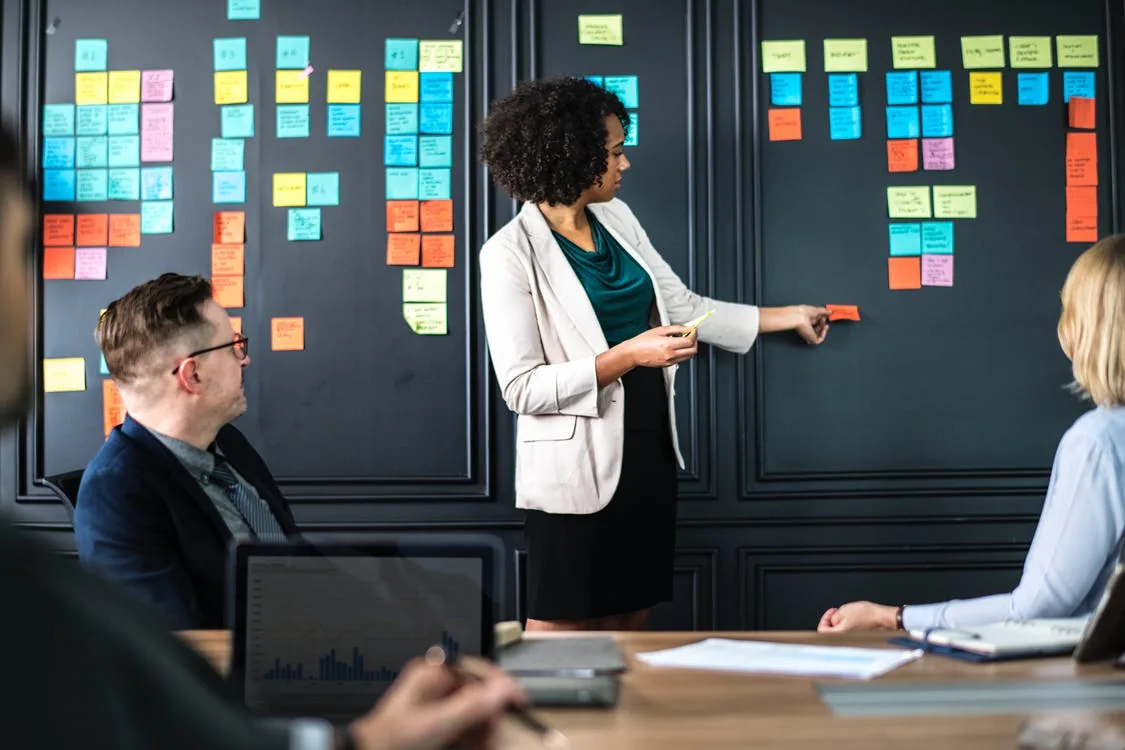 People discussing a wall covered in notes during a meeting