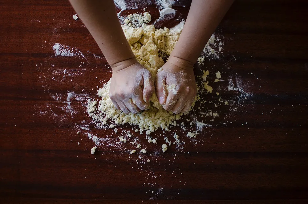 Hands kneading dough on a floured wooden surface