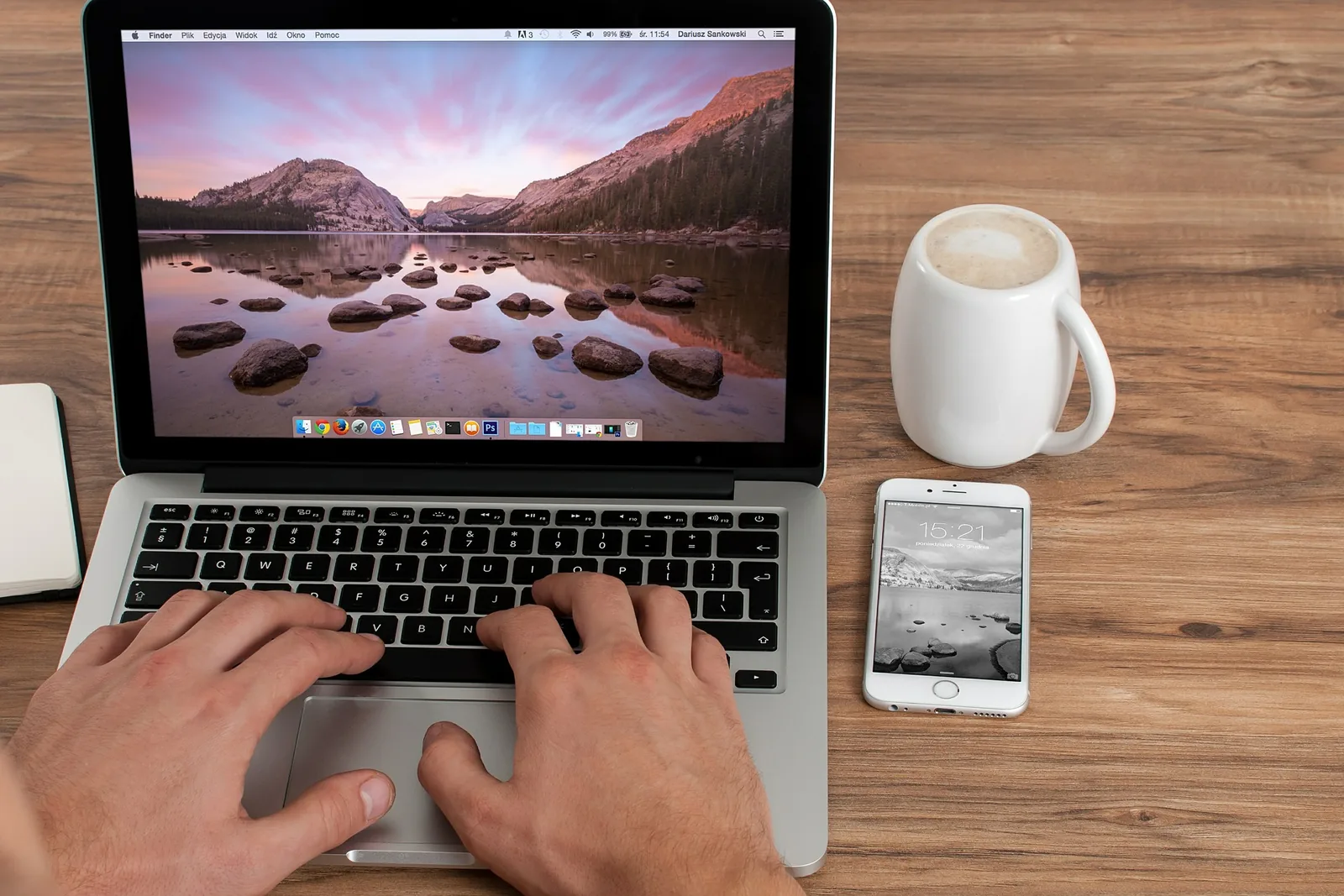 Hands typing on a laptop beside a phone and cup