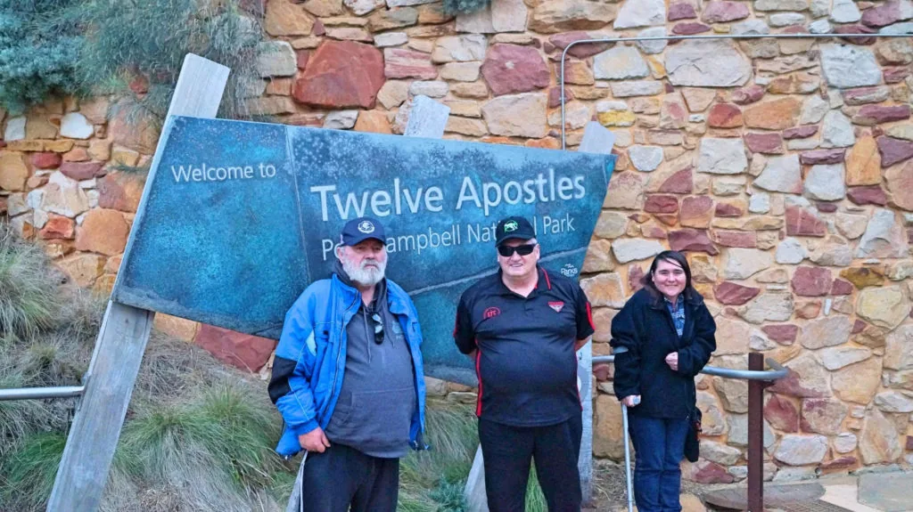 Three people standing in front of a sign that says 'Twelve Apostles'.