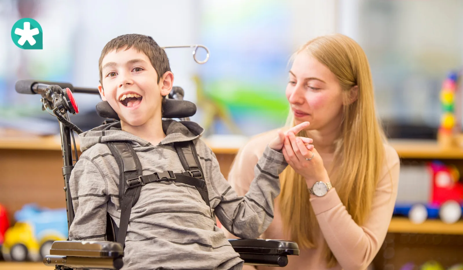 A child in a wheelchair beside an adult indoors