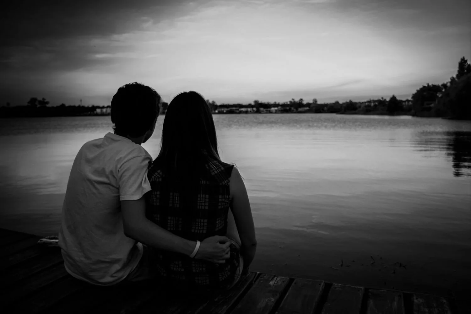 Two people sitting together beside the water at dusk