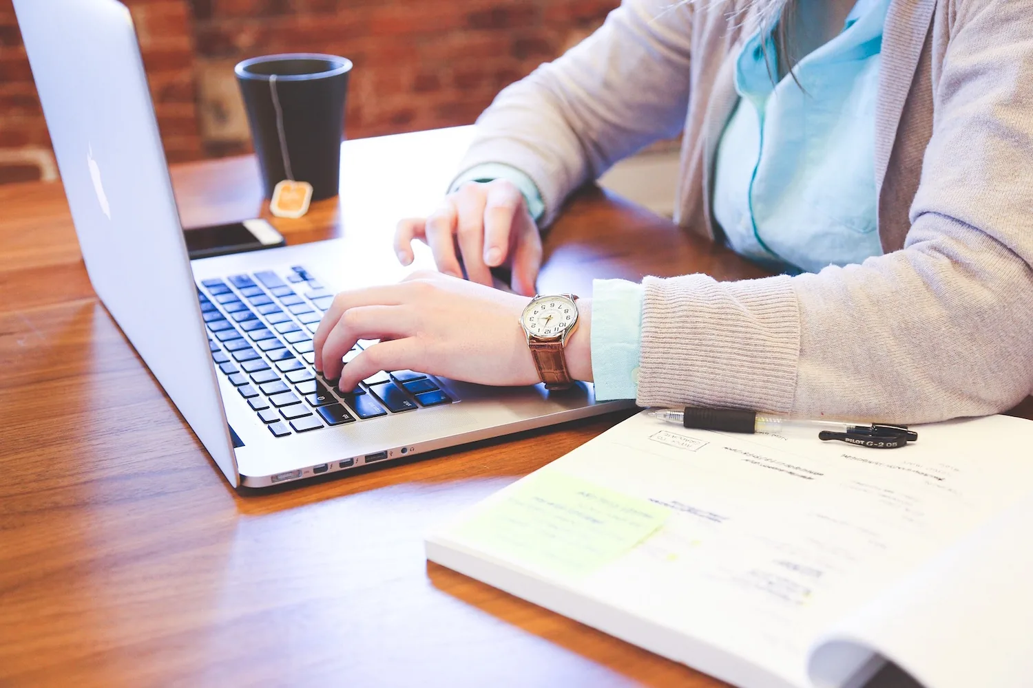 A person typing on a laptop beside documents