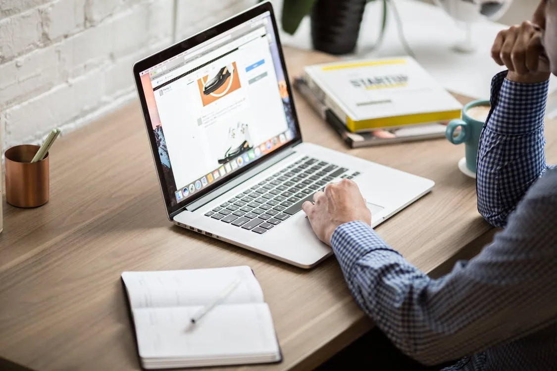 A person using a laptop beside a notebook