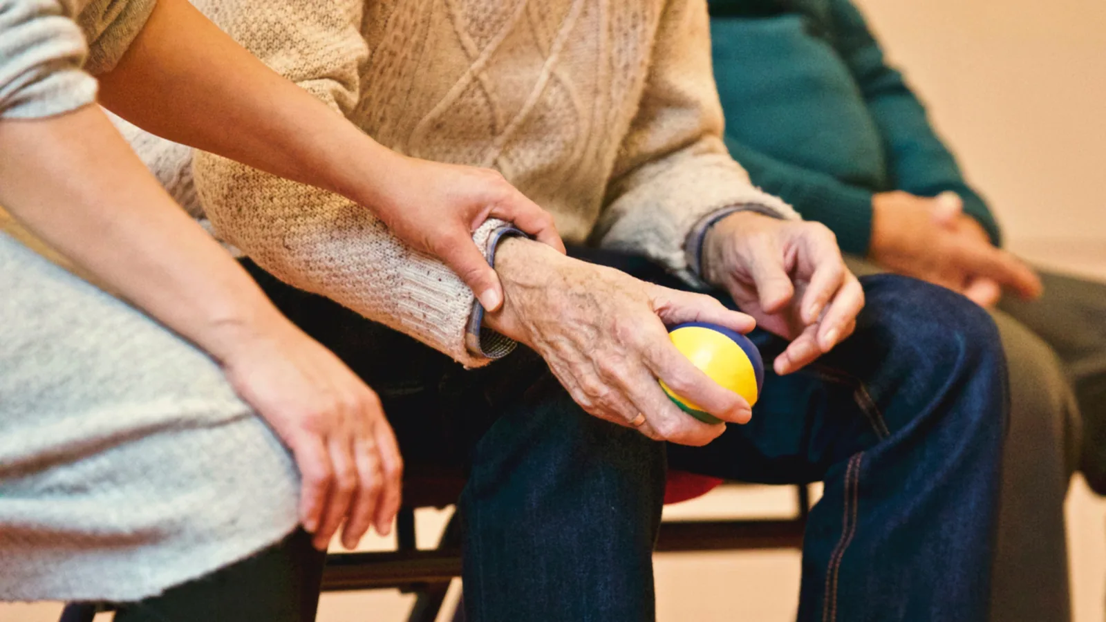 A seated person holding a tennis ball with another person’s hand near their arm