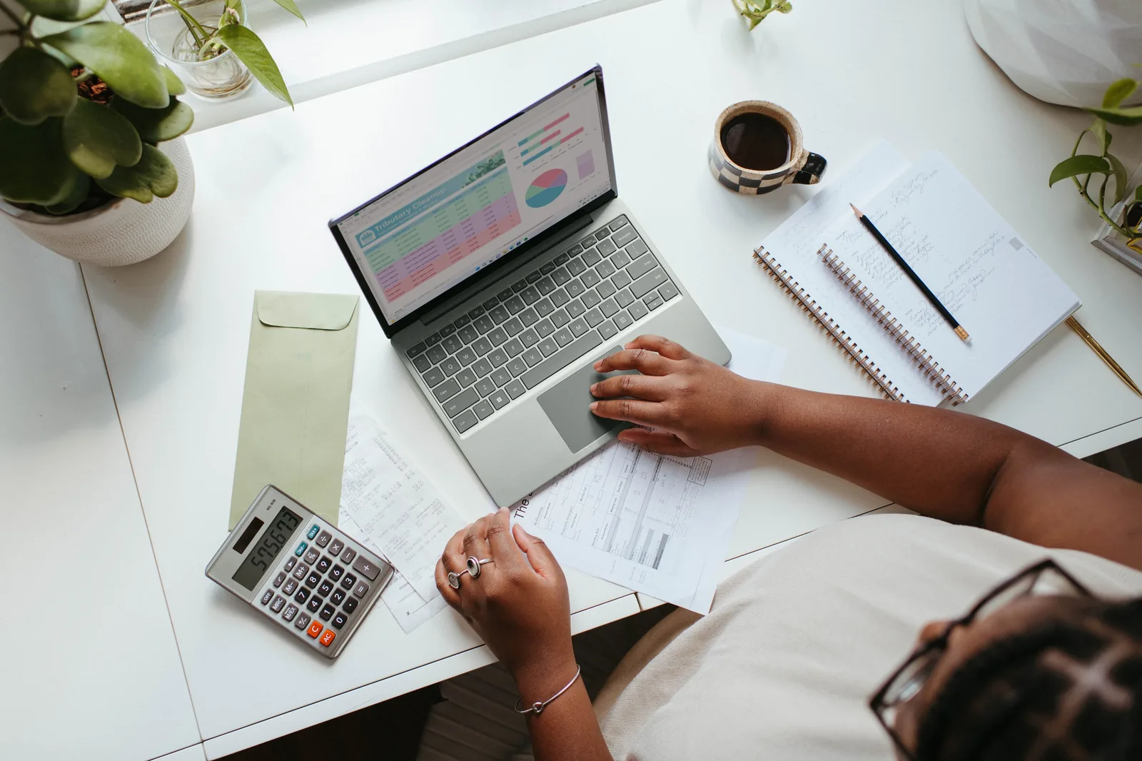 A person using a laptop beside a calculator and notebook