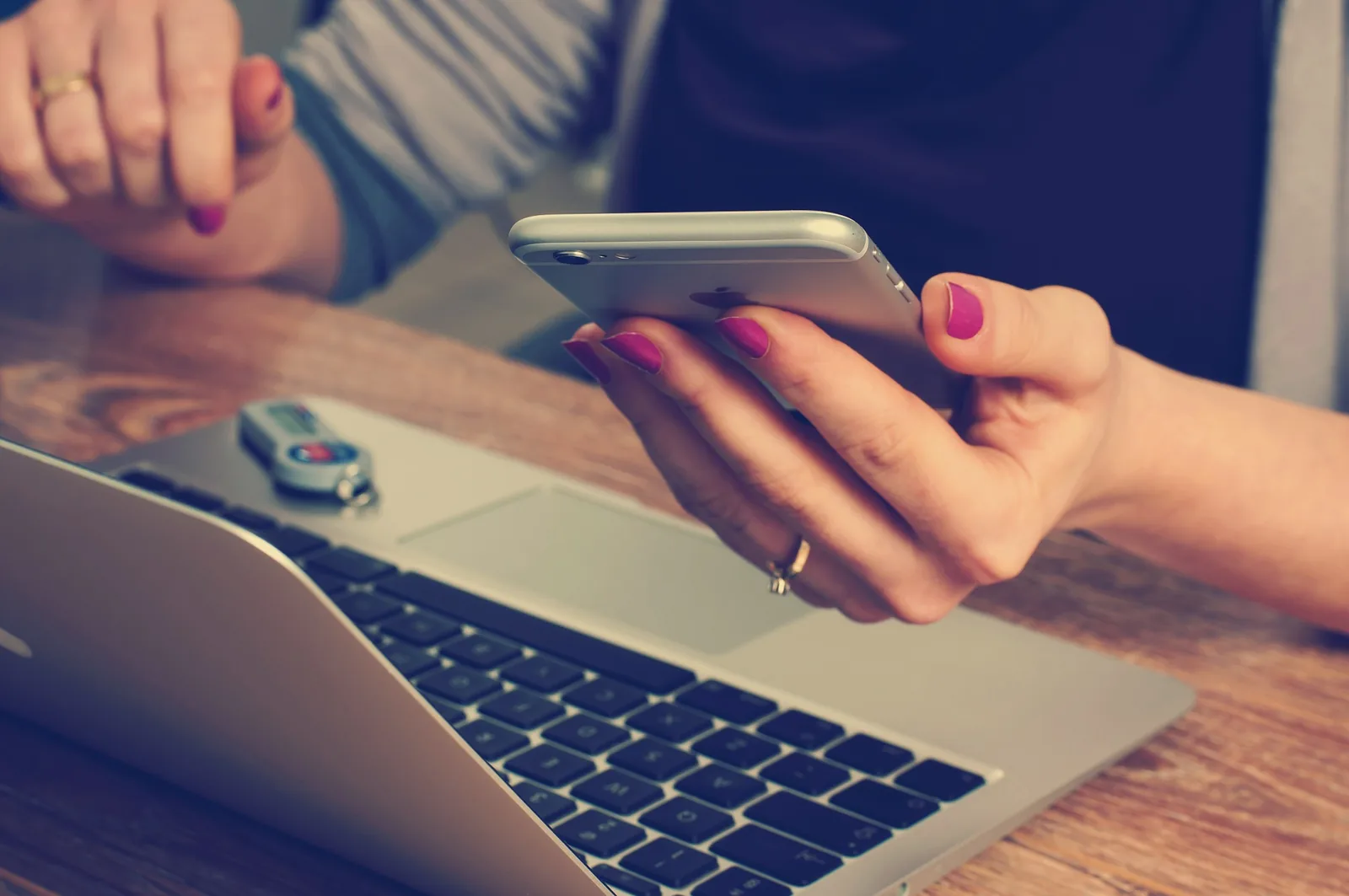 A person holding a phone beside a laptop