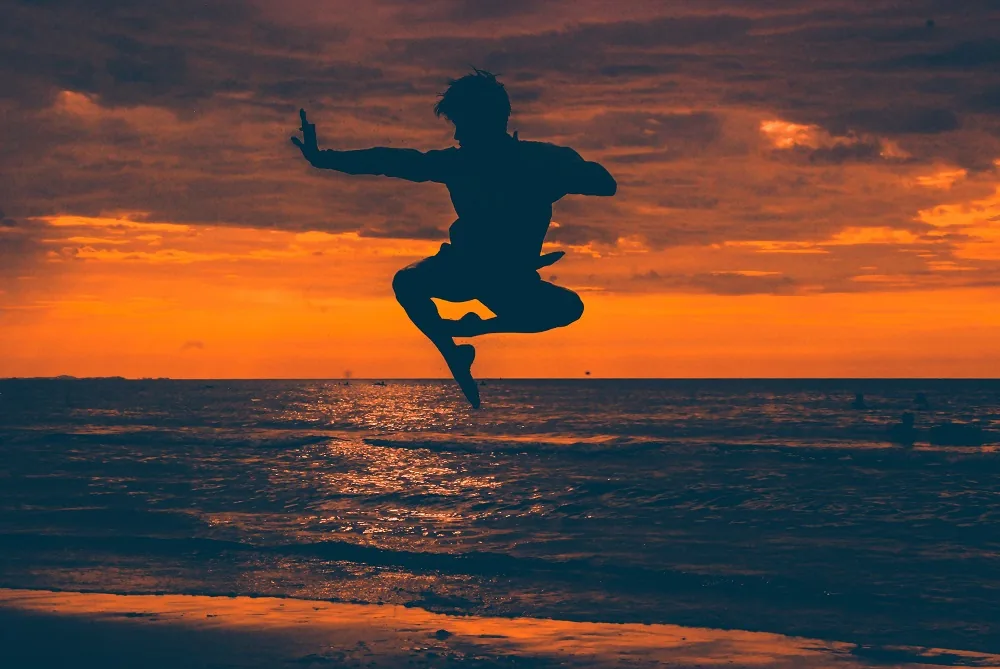 A person practising a martial arts pose on a beach at sunset