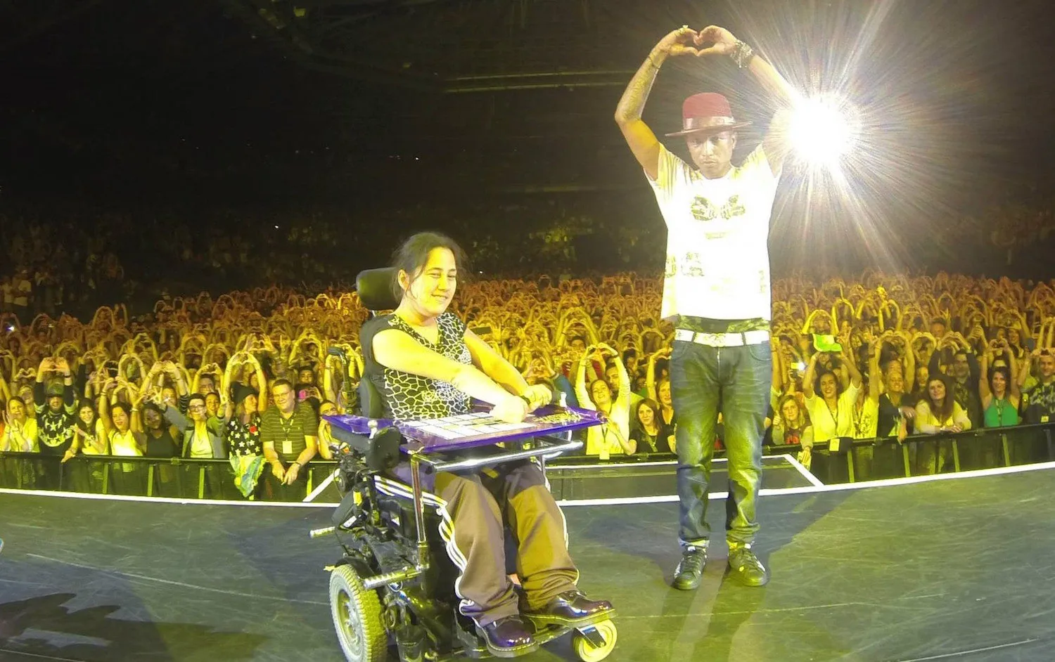 A wheelchair user beside a performer on a stage in front of a concert audience