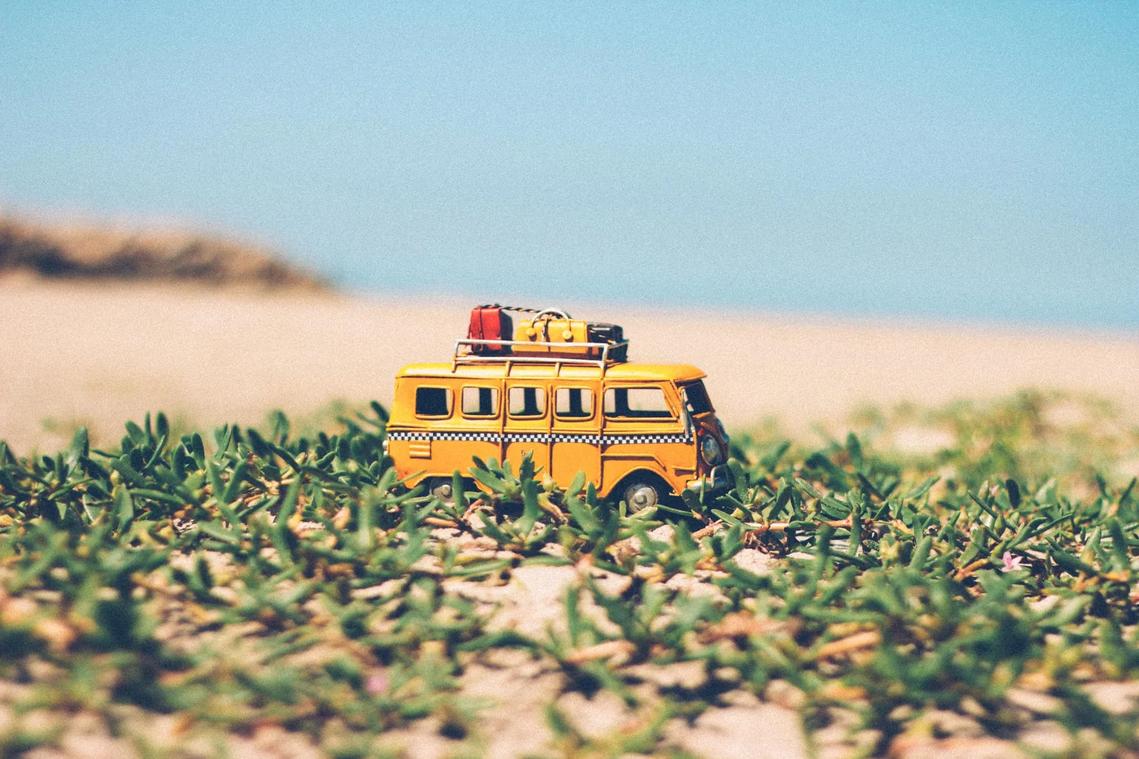 Small figurine of a yellow VW Combi by the beach.