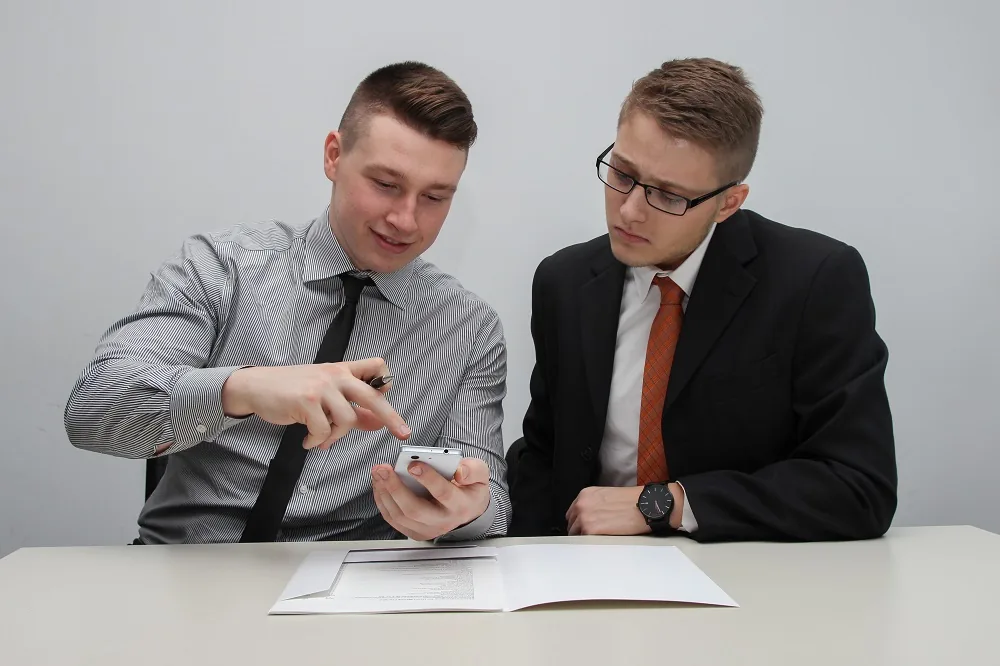 Two people discussing a small object above paperwork