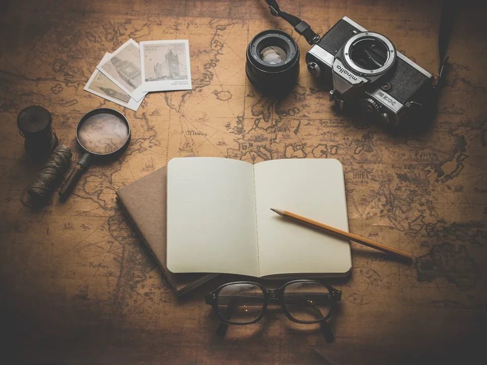 An open notebook beside a camera, compass and photographs