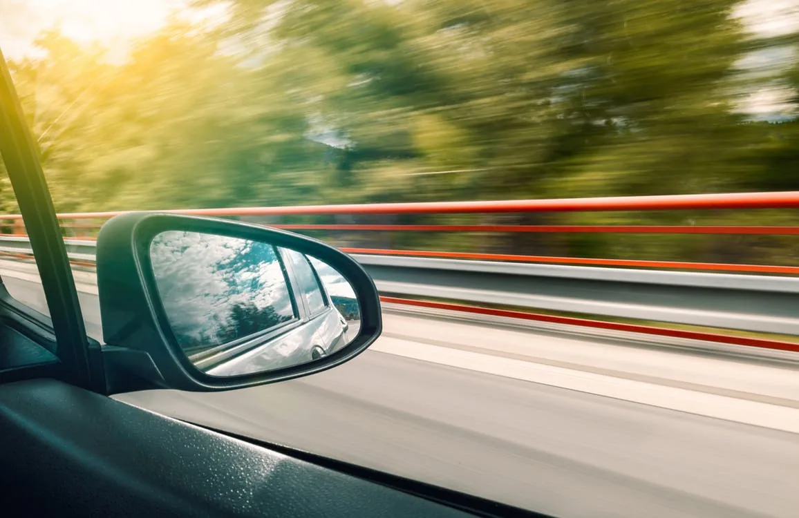View of a vehicle mirror beside a road with blurred trees
