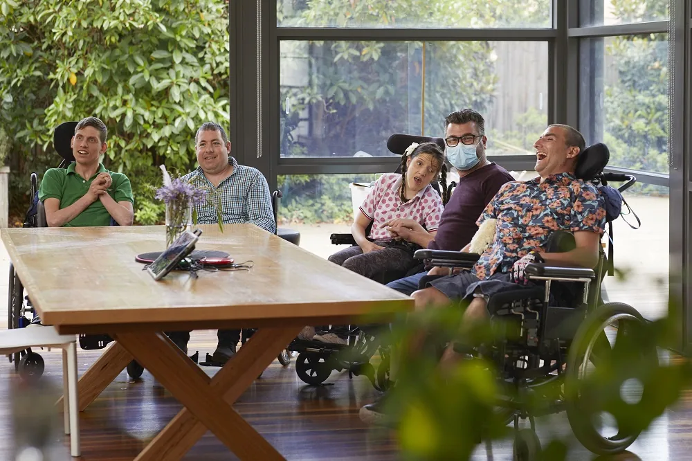 Five people gathered around a table, some using wheelchairs