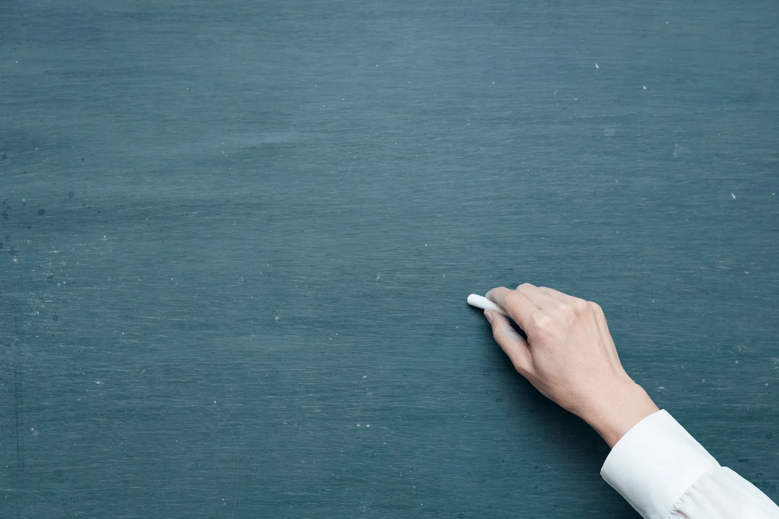 A hand holding chalk in front of a blank chalkboard