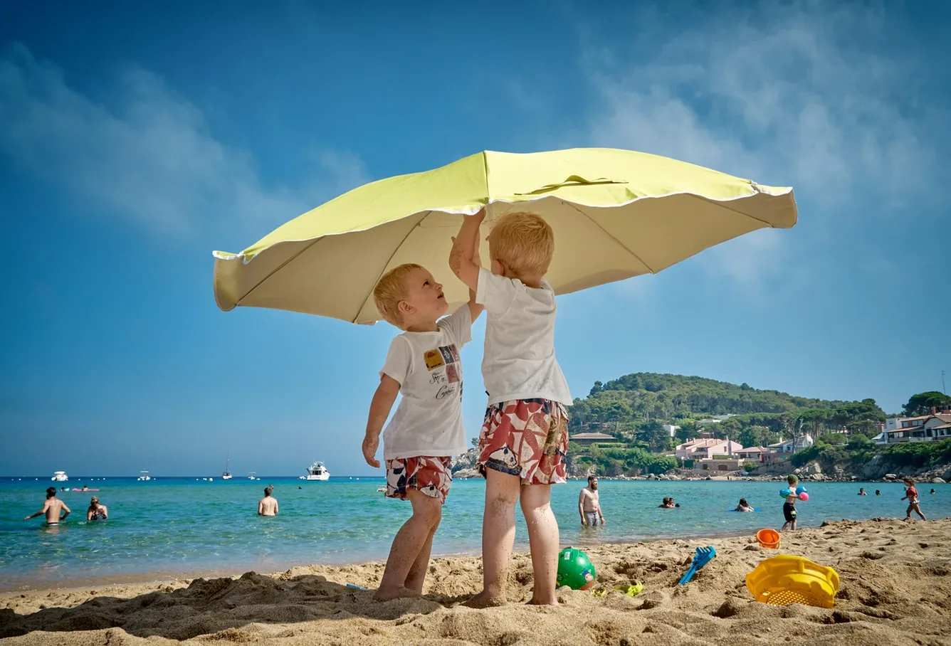 Two kids hoisting an umbrella on a beach