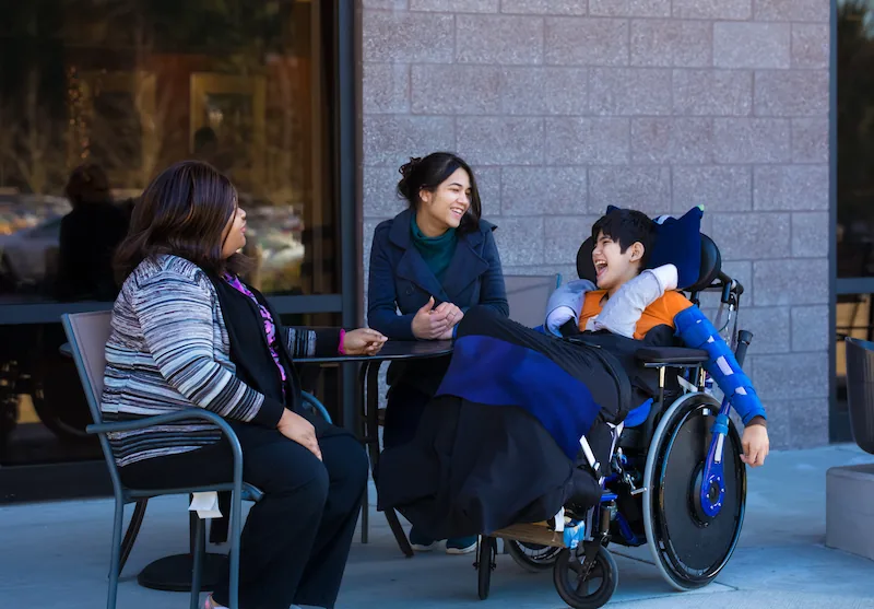 Three people, including a wheelchair user, talking outdoors