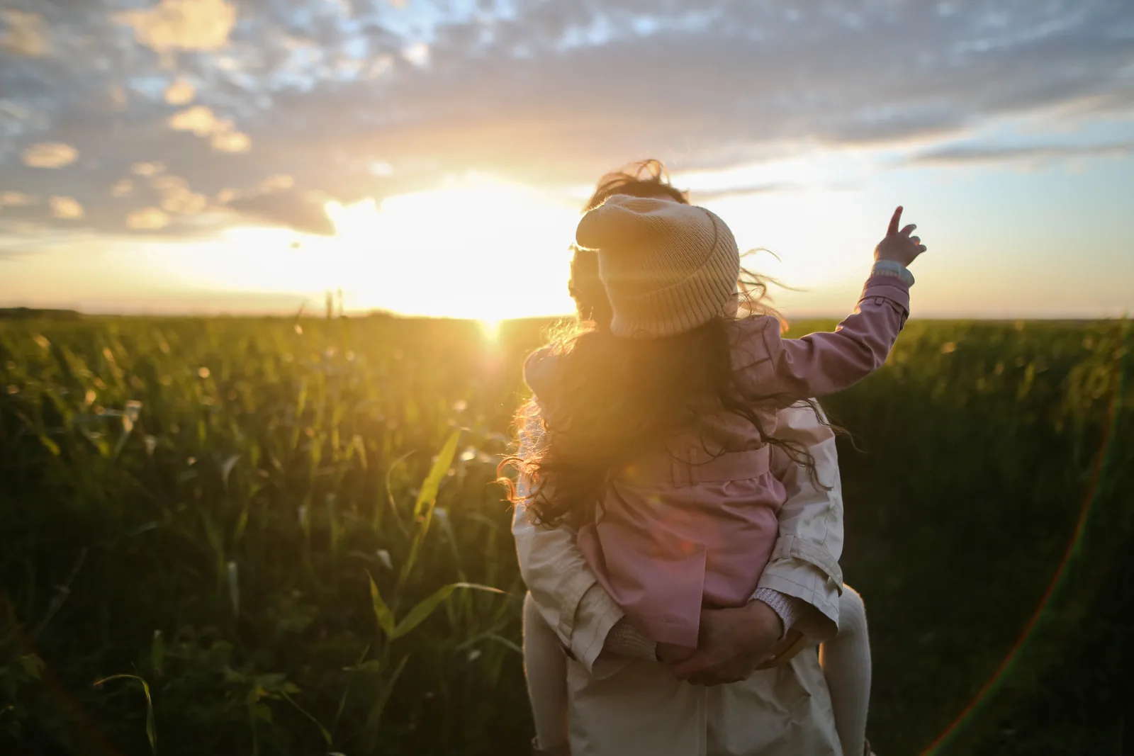 An adult carrying a child outdoors at sunset