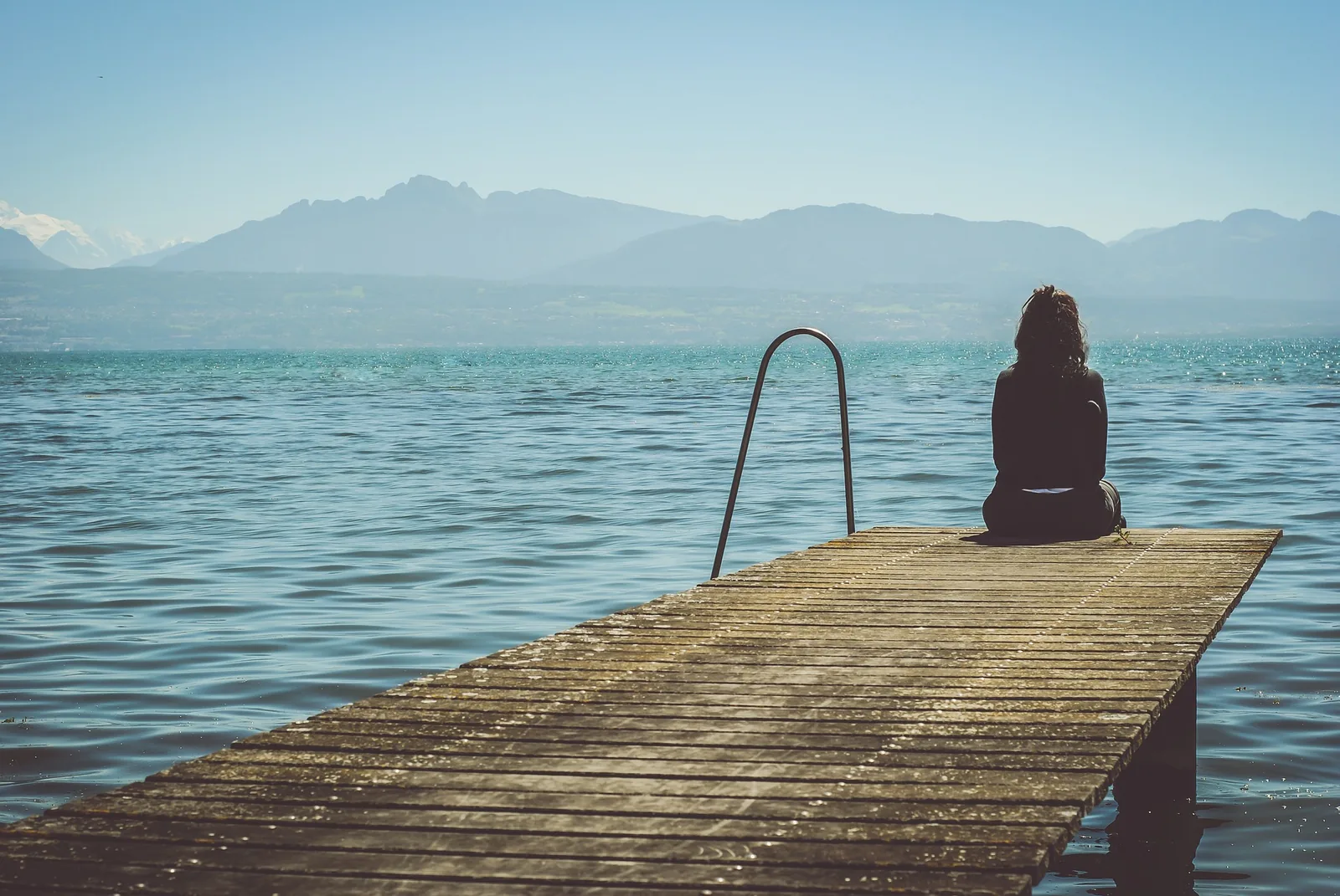 A person seated on a jetty beside water