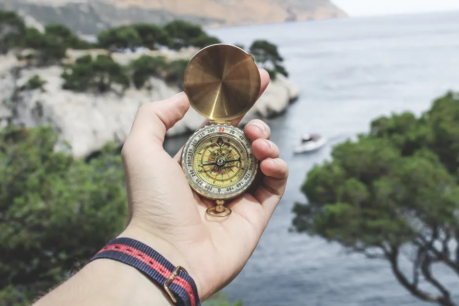 A hand holding a compass beside the coast