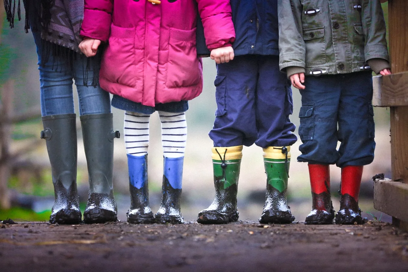 Children standing in gumboots on a muddy path