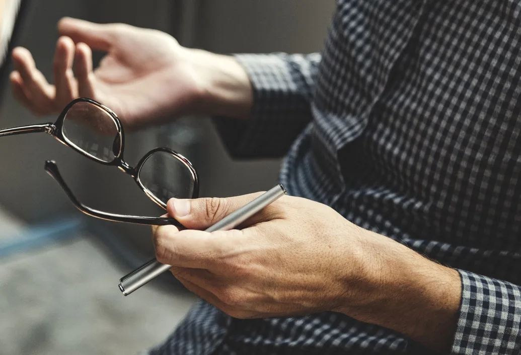 A pair of hands holding glasses and a pen.