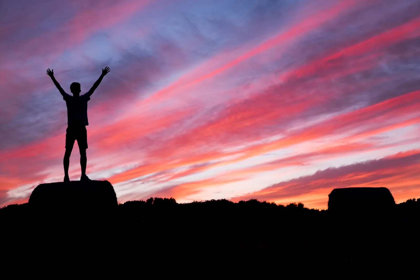 Silhouette of a person with raised arms beneath a colourful sky