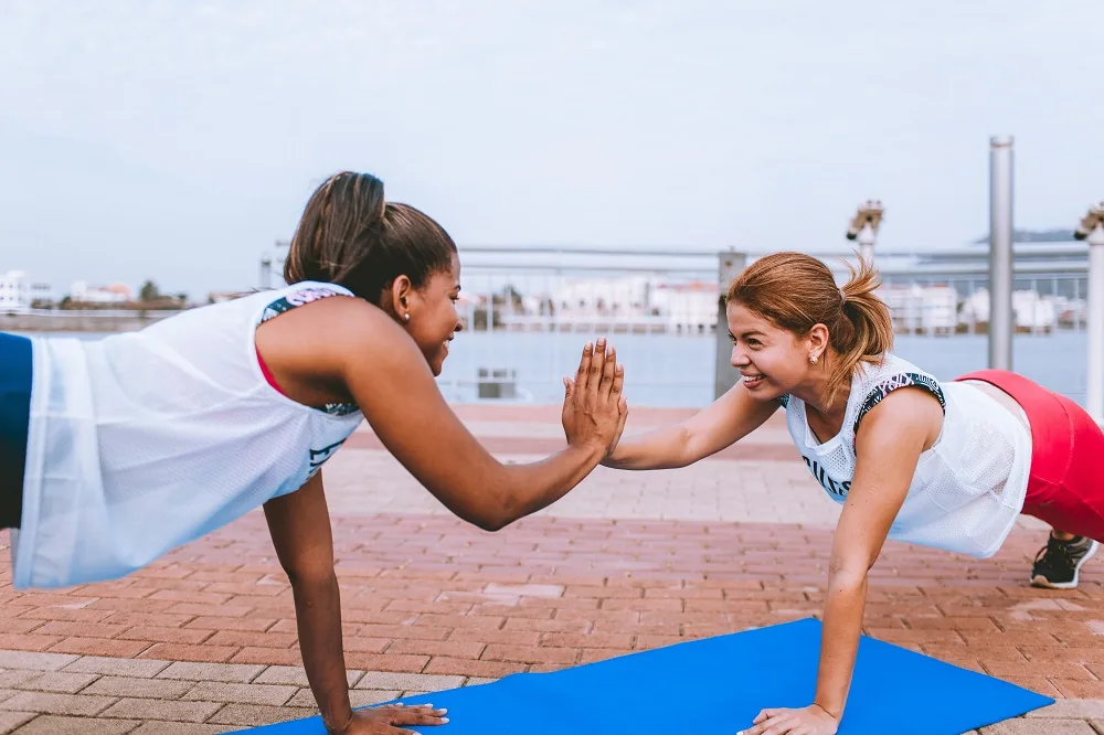 Two people exercising on mats outdoors and touching hands