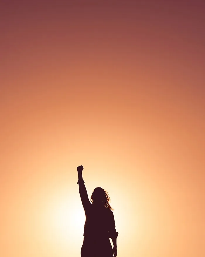 Silhouette of a person raising an arm against an orange sky
