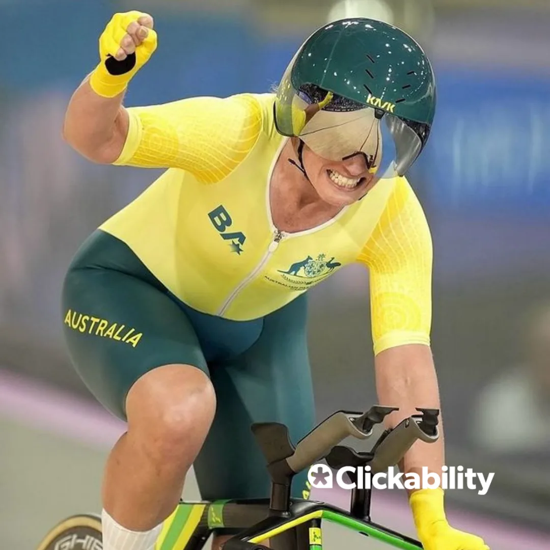 A woman raising her hand in celebration while cycling in a velodrome. 