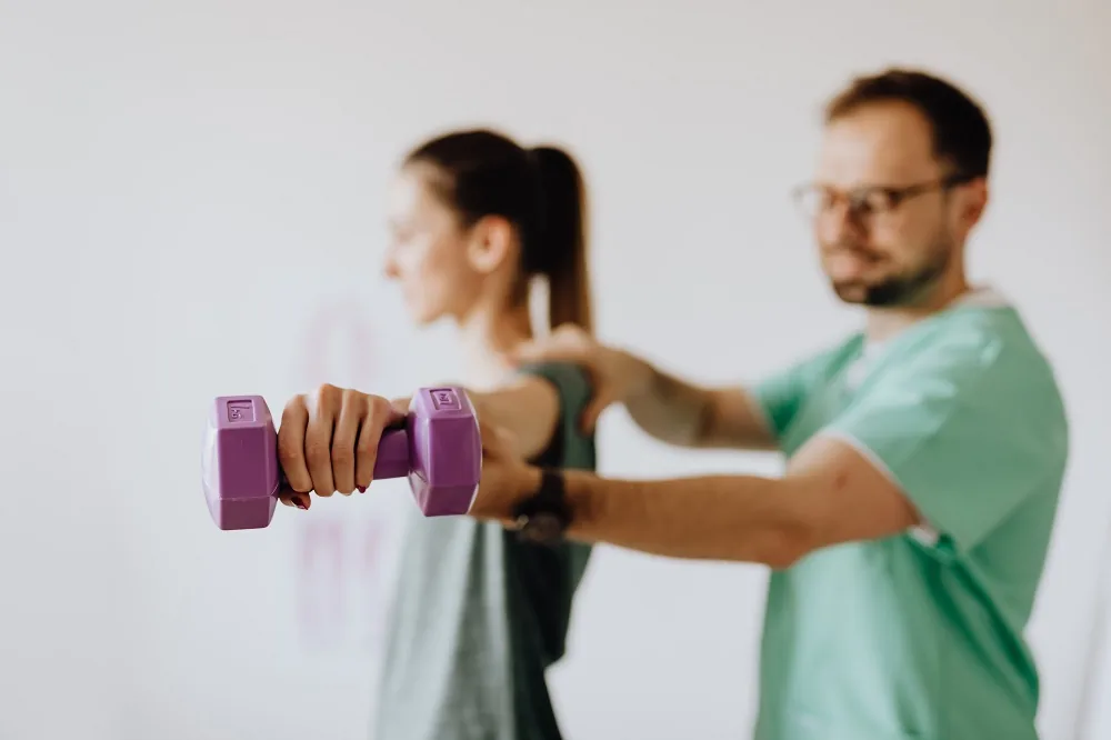 A person assisting another person who is holding dumbbells