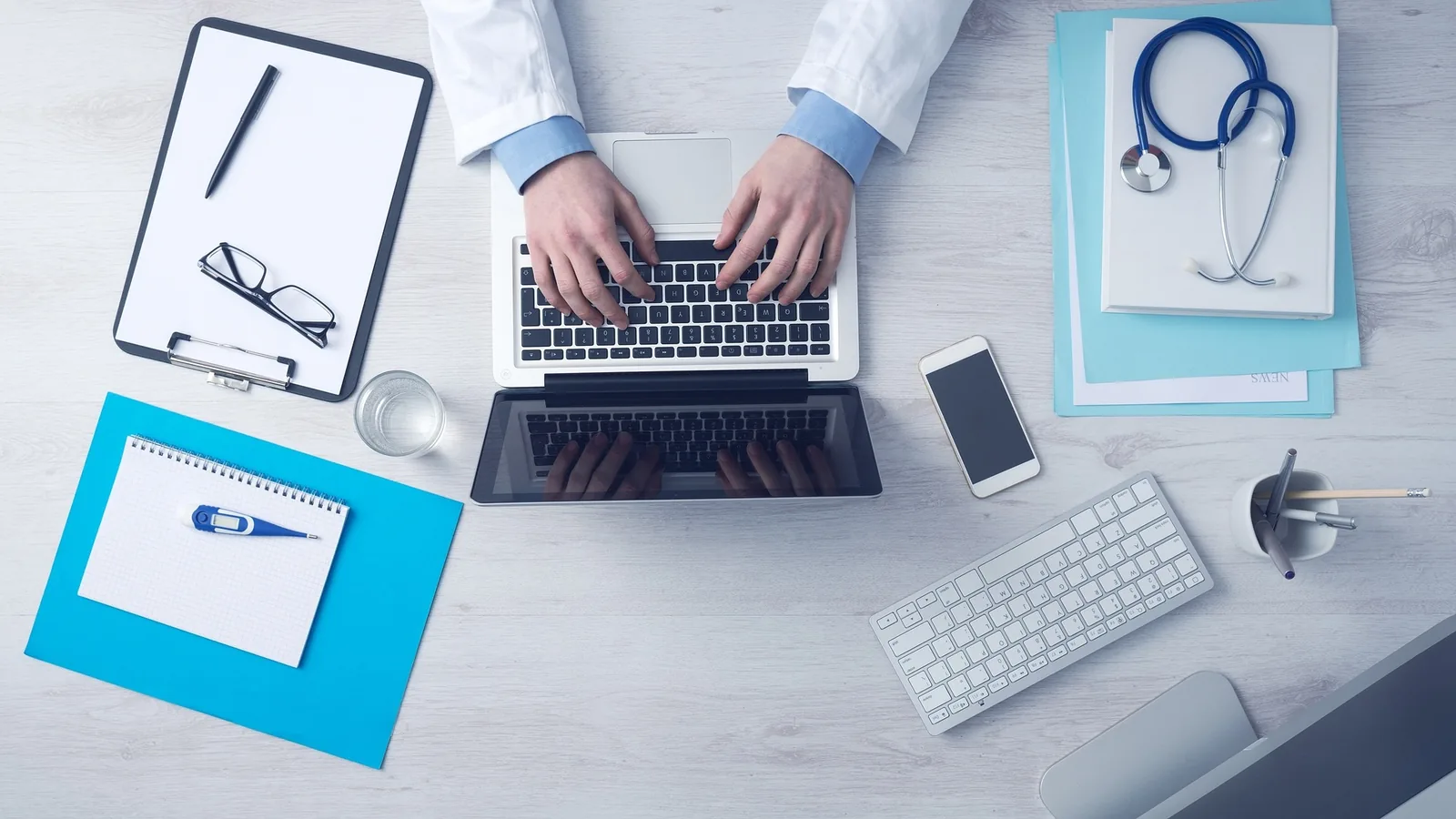 A person using a laptop beside medical equipment and paperwork