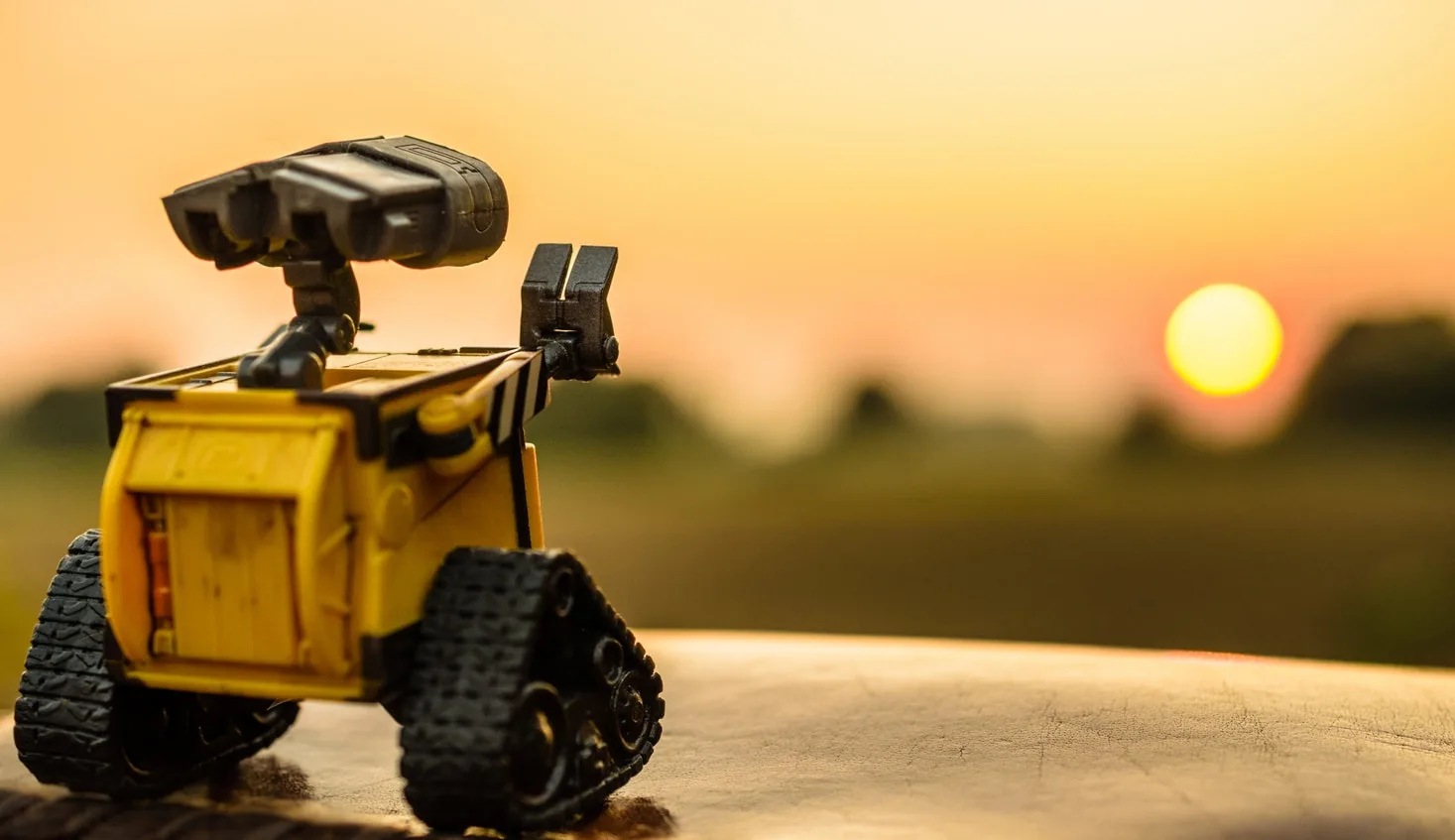 A toy robot on a surface in front of a sunset