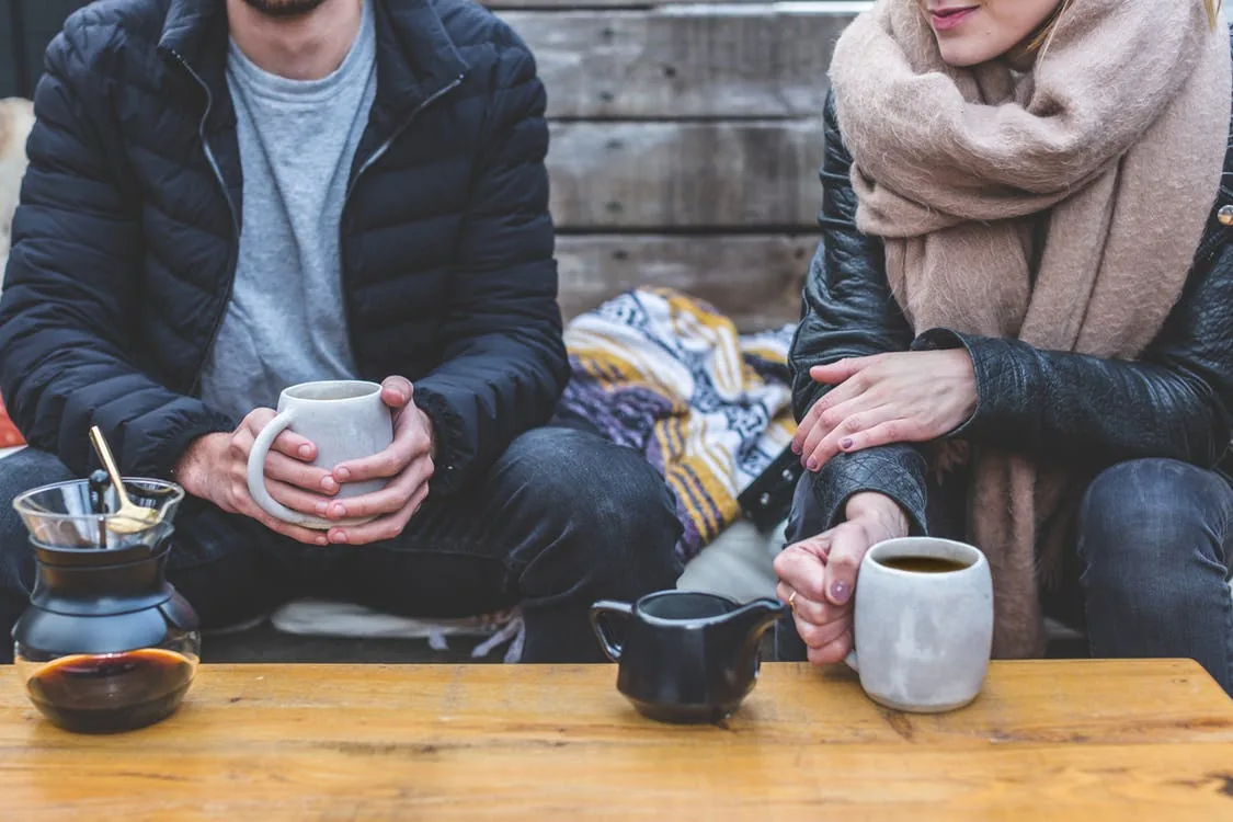 Two people sitting outdoors with cups of coffee