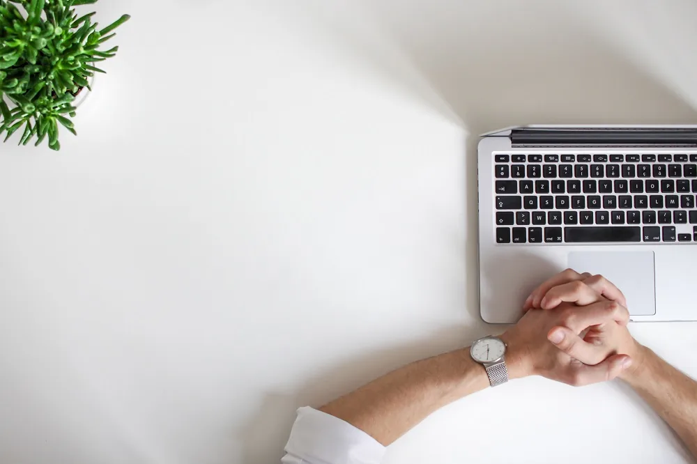 Clasped hands beside a laptop on a desk