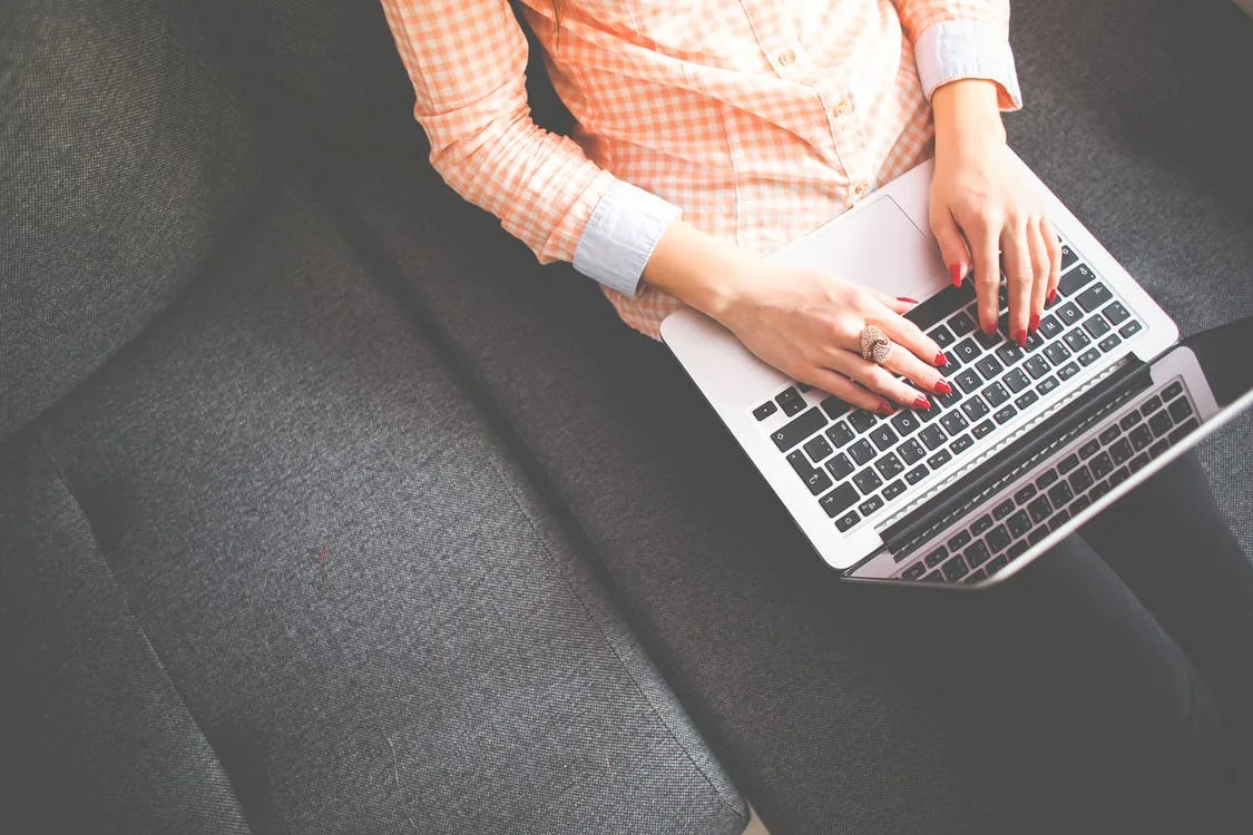A person typing on a laptop resting on their legs