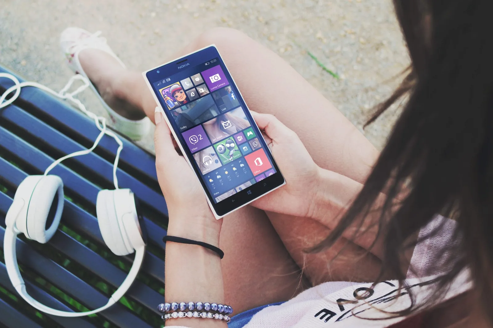 A person using a smartphone outdoors beside headphones and a bag
