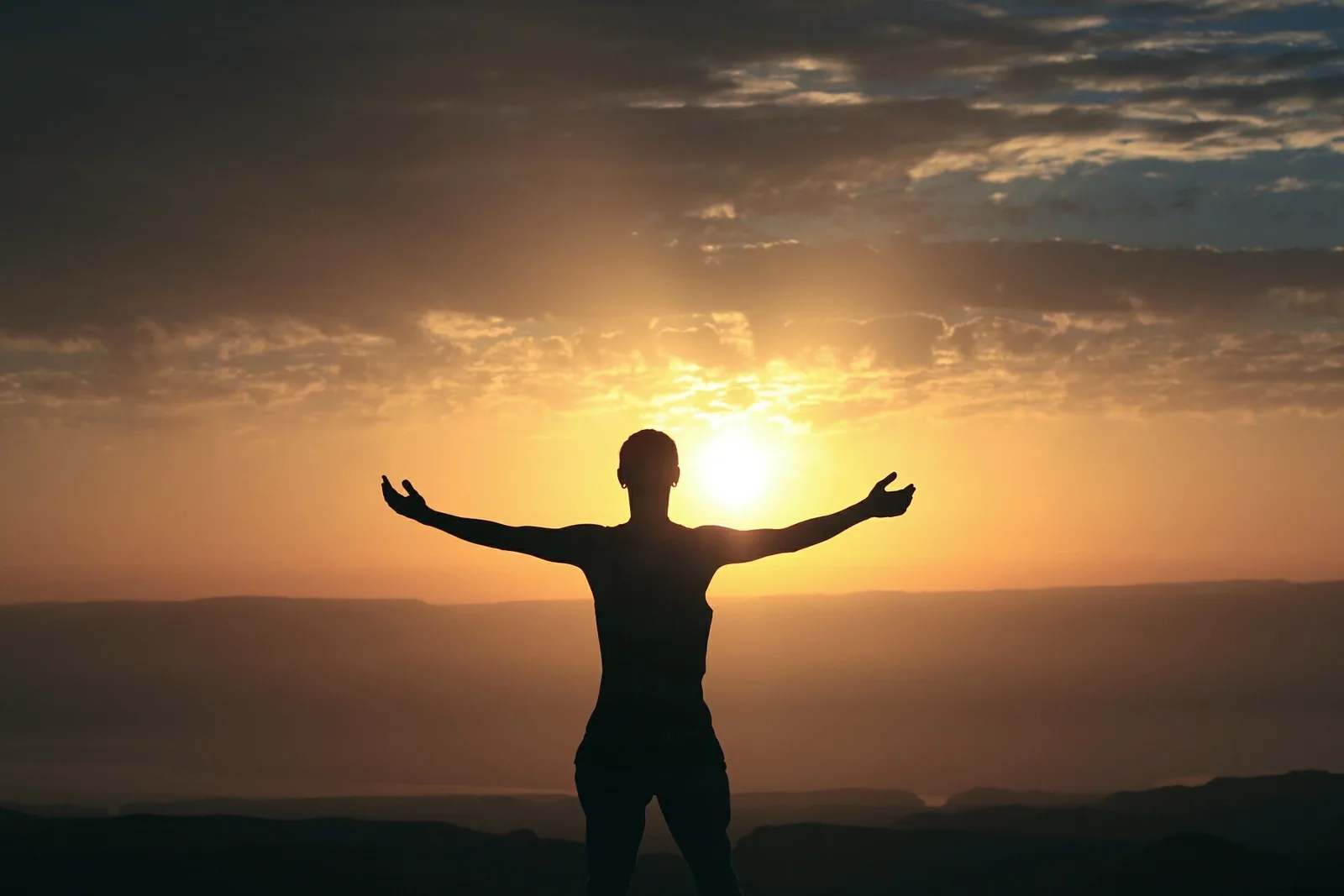 A person with arms outstretched against a sunset sky