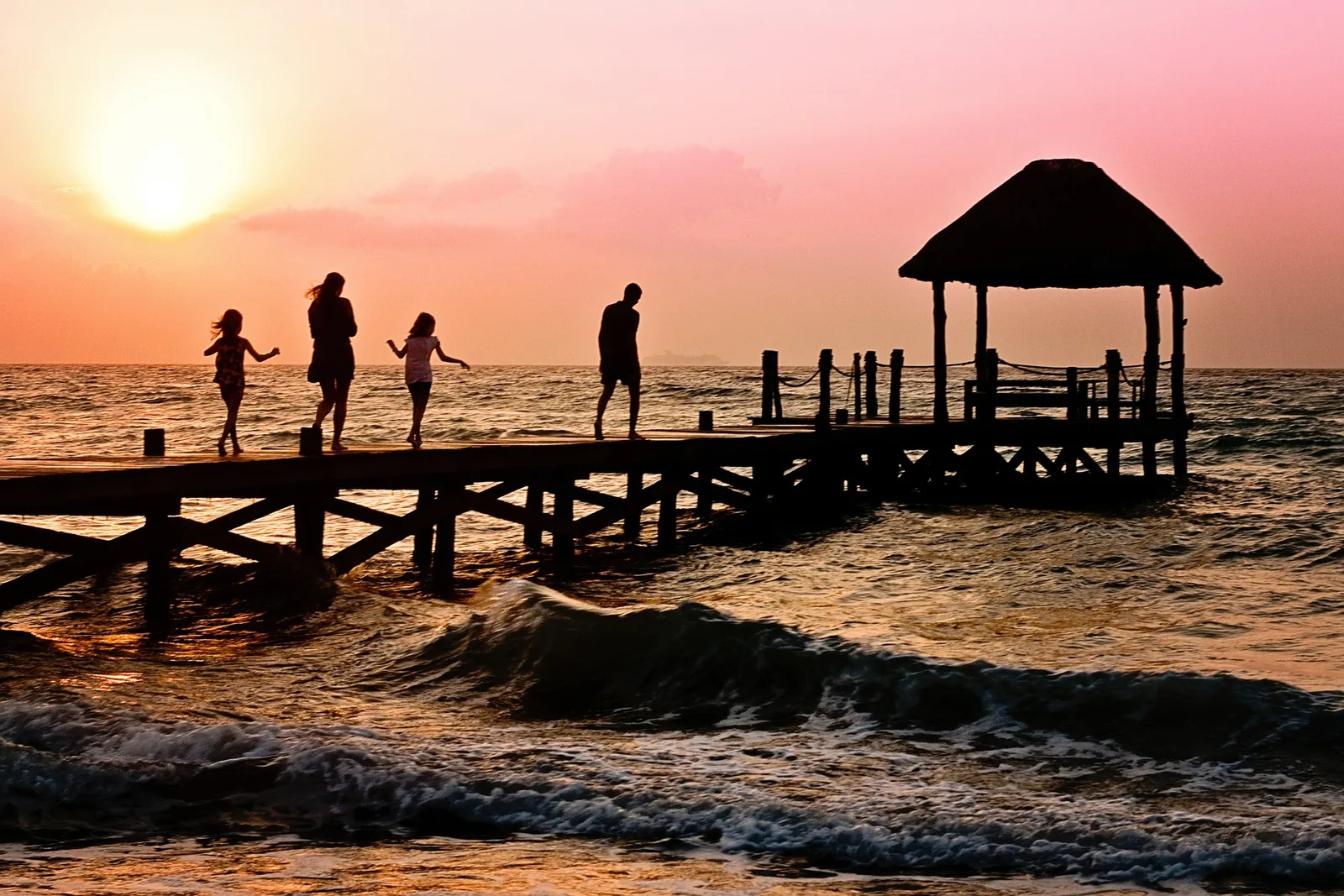 People on a jetty beside the sea at sunset