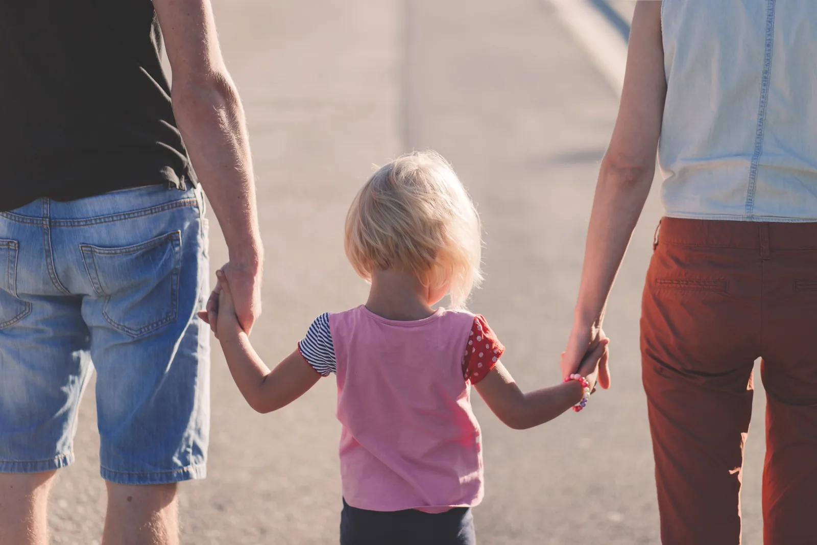 A child holding hands with two adults outdoors
