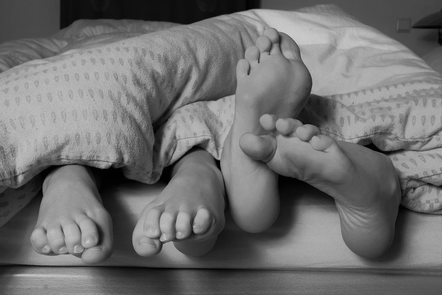 Two people’s feet resting together on a bed