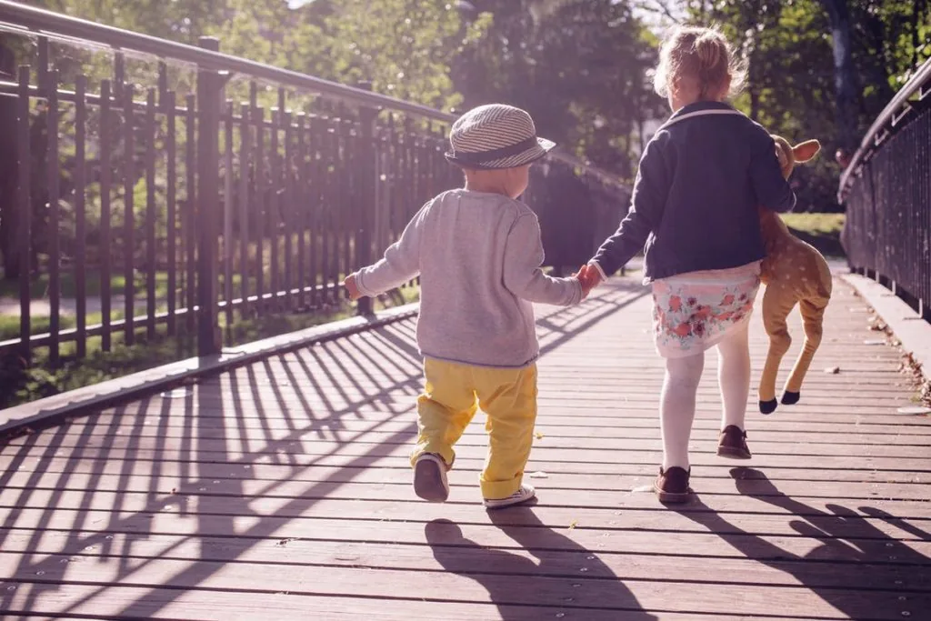Sister leading her younger brother across a bridge
