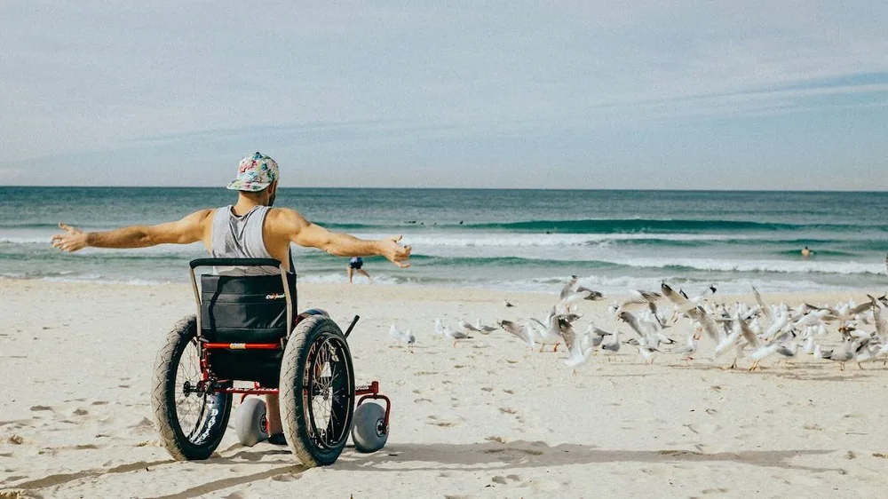 A wheelchair user facing the sea on a sandy beach