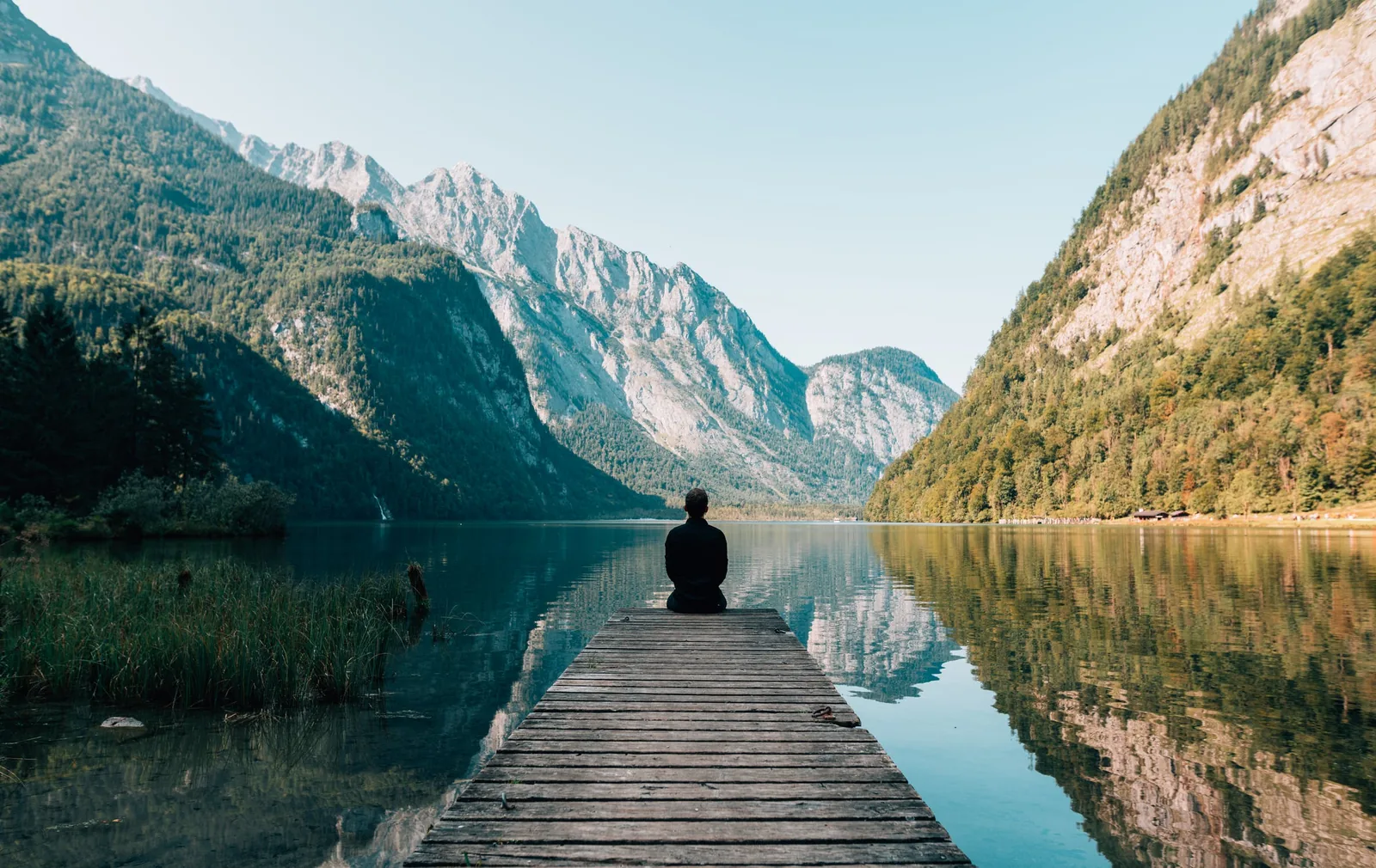A person sitting on a dock facing a mountain lake