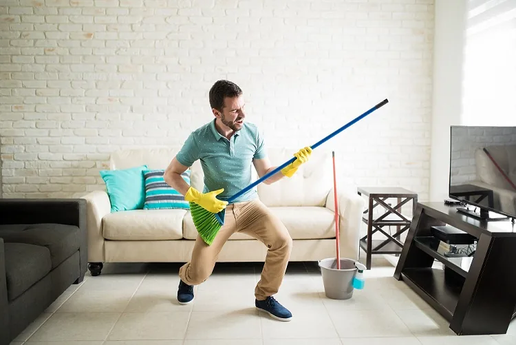 A person holding a broom like a guitar in a living room