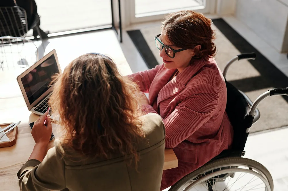 Two people looking at a tablet, one seated in a wheelchair
