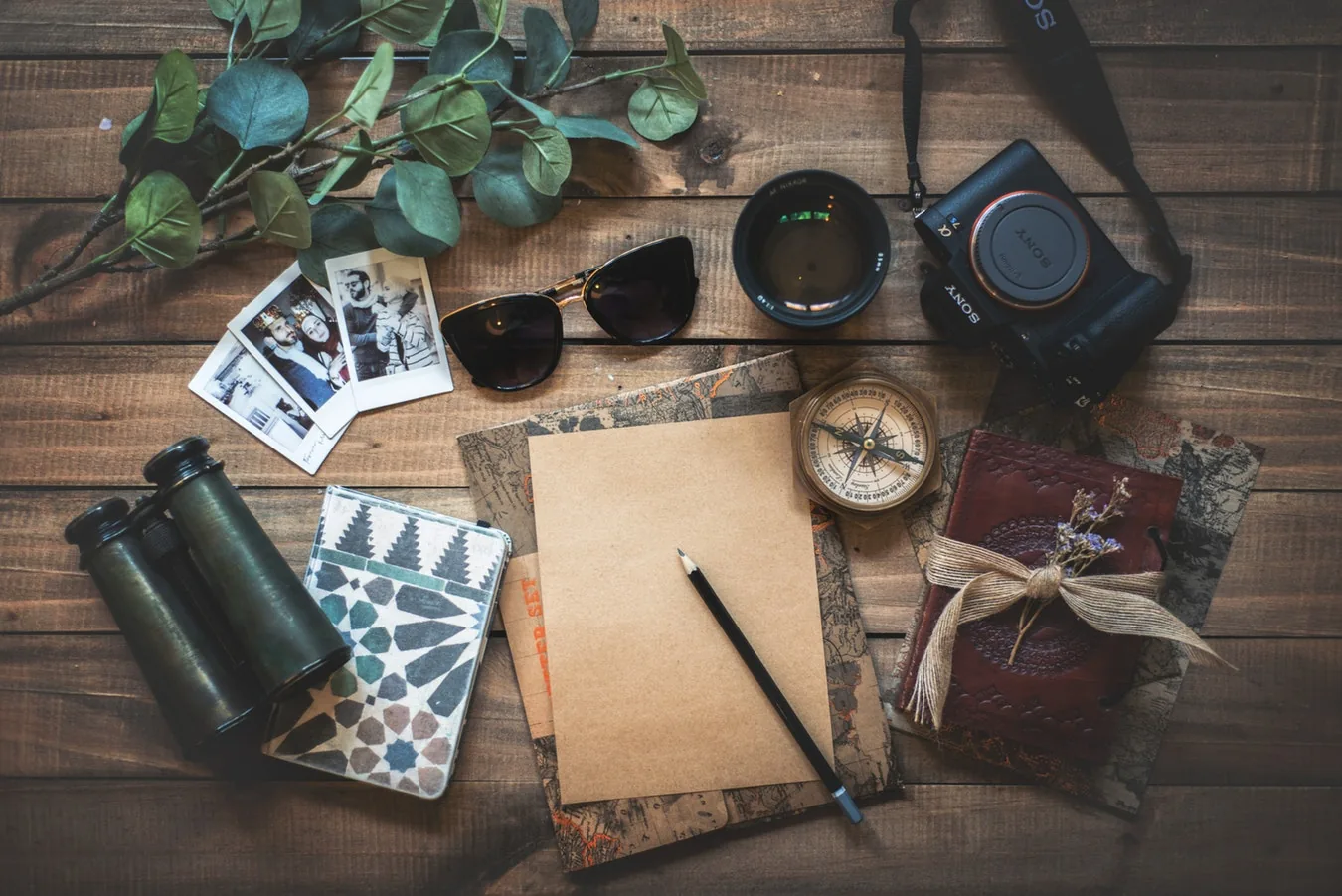 Travel items including a notebook, camera and binoculars arranged on a table